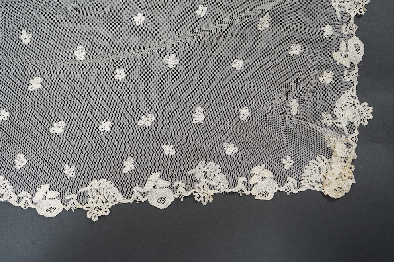 An Edwardian Brussels bobbin lace on net wedding veil, with all over bobbin lace appliqué spot motifs, within an ornate bobbin lace border, approximately 175cm x 168cm. Condition - there are various rust stains and holes